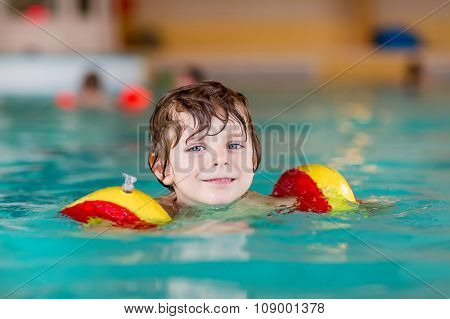 little kid boy with swimmies learning to swim in an indoor pool