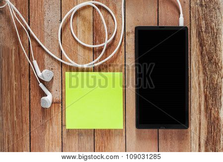 Closeup Of Black Smartphone With Headphones And Sticky Notes On Wooden Surface