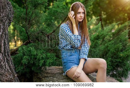 Young woman cute brunette girl sitting on stone headphones