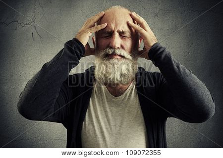emotional bearded man holding his head and wincing in pain over grey background