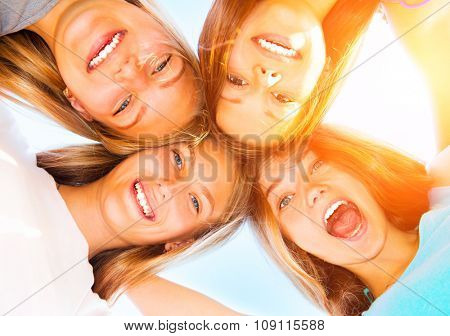Girlfriends staying together, looking at camera and laughing over blue sky. Group of Four Teenage Girls having fun outdoors. Friendship concept. Group of smiling Joyful girlfriends making a huddle