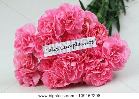 Feliz cumpleanos (Happy birthday in Spanish) card with pink carnations on rustic surface