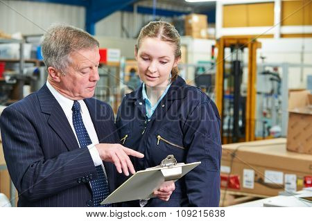 Factory Manager And Apprentice Engineer Looking At Clipboard