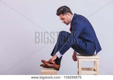 handsome man in suit sitting on chair in studio cleaning his brogue shoes