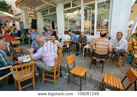 Senior Men Sitting Around Tables And Talking In Rustic Cafe Of Village