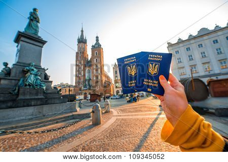 Female hands holding Ukrainian abroad passports on the Krakow city center background