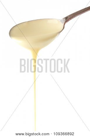 Condensed milk pouring from a spoon, isolated on white
