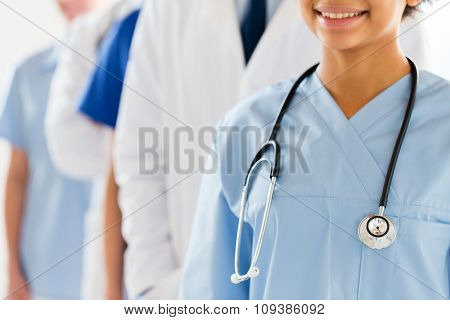 health care, profession, people and medicine concept - close up of happy female doctor or nurse with stethoscope over group of medics at hospital