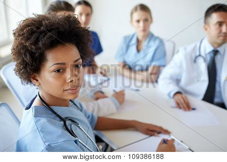 health care, profession, people and medicine concept - african american female doctor or nurse over group of medics meeting at hospital