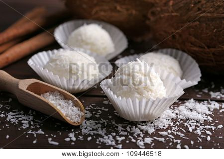 Candies in coconut flakes and fresh coconut on dark wooden background