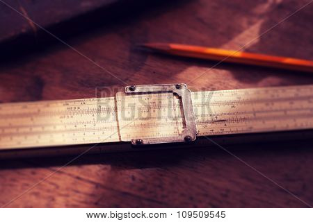Calculation. Vintage calculating slide rule and pencil, on old desk. Intentionally shot in retro muted color. Shallow depth of field.