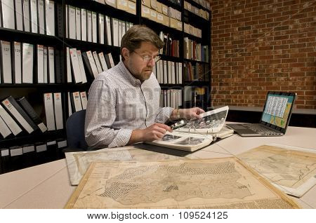 Researcher In Archive Examining Maps And Other Archival Materials
