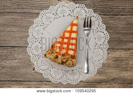 Fresh tasty sweet piece of  carrot cake on a white lace napkin and a dessert fork on a wooden background.