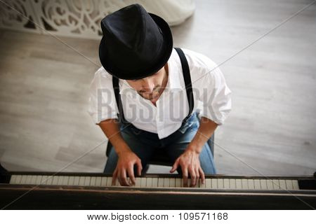 Handsome young man in hat making piano music, topside view