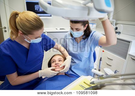 people, medicine, stomatology and teeth care concept - happy female dentist with assistant checking patient girl dental occlusion teeth at dental clinic office