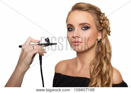 portrait of a beautiful young blonde woman on a light background. there is hand with aerograph makin