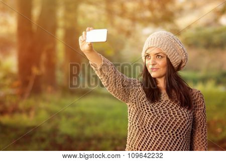 Young woman taking a selfie in park in autumn