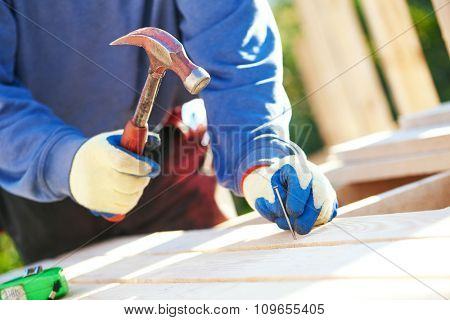 A closeup of male carpenter worker hands hammering nail into board outdoors