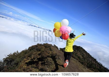 young woman with balloons on mountain peak