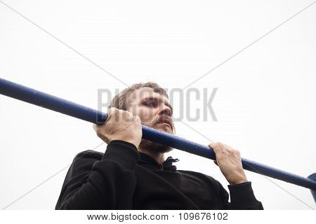 young man doing pull ups on horizontal bar outdoors