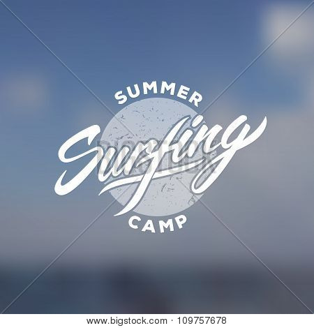 Vintage surfing camp emblem with hand drawn elements on blurred sea photo.