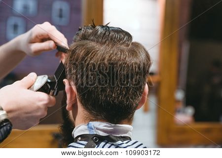 Closeup of barbers hands making short haircut to man using trimmer in barbershop