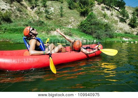 A male and female in a red inflatable canoe celebrating reaching calm waters of a river.