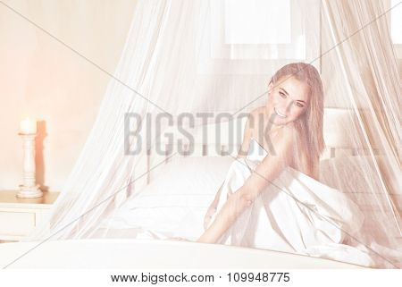 Romantic woman sitting in the bed under gentle transparent valance, spending weekend in luxury spa hotel, enjoying rest and relaxation