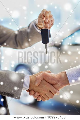 auto business, car sale, deal, gesture and people concept - close up of dealer giving key to new owner and shaking hands in auto show or salon over snow effect