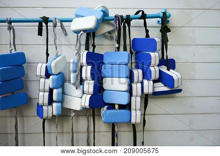 A Row Of Swimming Belts Hanging On Pvc Bar By Swimming Pool Against White Pattern Wall.