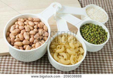 Foods High in Carbohydrate Raw Pasta Rice Peanuts and Mung Beans in Plastic Measuring Cups.