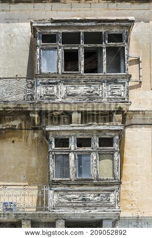 Building with traditional maltese balcony in historical part of Valletta. Damaged windows on the facade of a abandoned house in Malta