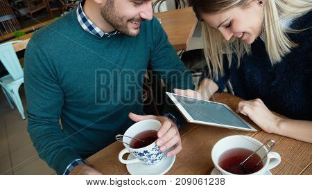 Young attractive man and beautiful woman on date looking on tablet in coffee shop