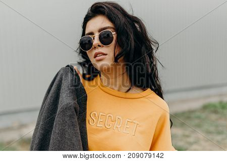 Portrait of stylish modern young curly woman in coat sunglasses