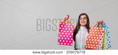 The brunette woman in a shirt and skirt with a packeges in hands on a gray background. Place for text.