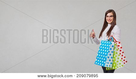 The brunette woman in a shirt and skirt with a packeges in hands on a gray background. Place for text.