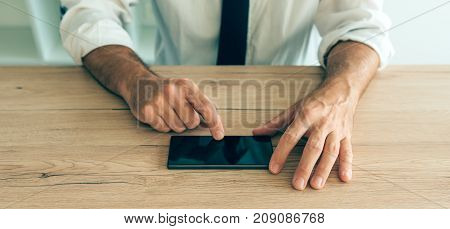 Smartphone in hands of successful businessman. Adult caucasian business person in white shirt with tucked rolled up sleeves using mobile phone at the desk in office.