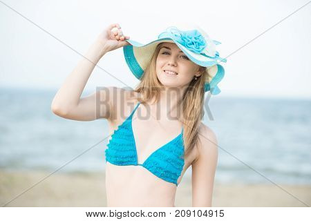 Young lady sunbathing on a beach. Beautiful woman posing at the summer sand beach. Outdoor summer portrait of pretty sport style woman in blue bikini. Ocean sea coast. Beautiful fit tan girl. Sexy slim model caucasian ethnicity outdoors.