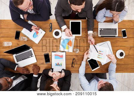 Multiethnic team meeting top view. Manager and emploees listen to the report in comfortable office, top view of wooden table