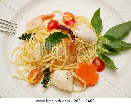 Spaghetti stir fried. It has a spicy taste with shrimp and squid in white plate.