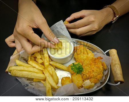 The woman eating french fries and nuggets. She dipping on mayonnaise sauce taste more delicious.