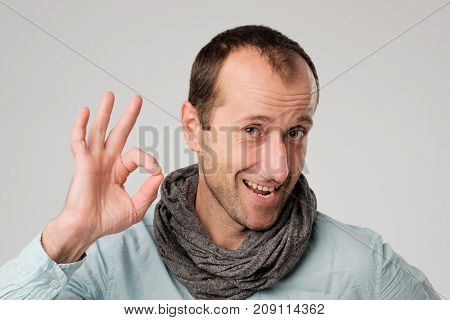 happy spanish man shows OK against gray background. He is wearing scarf after illness. Now he is healthy