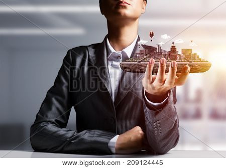 Cropped image of businessman in suit presenting in his hand modern city block with office view on background. 3D rendering.