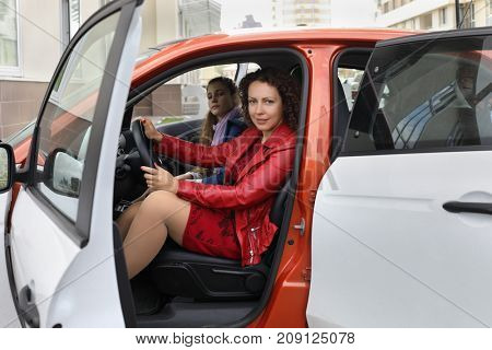 Beautiful curly woman with girl sit in white small car outdoor, focus on woman