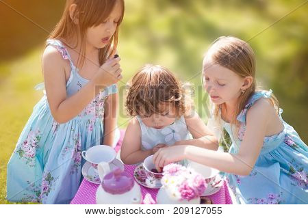 Adorable three little sisters girls dressed like princesses playing tea party. Beautiful decorated tea party outdoors at the backyard.