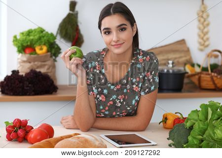 Young latin  woman is making online shopping by tablet computer while holding green apple. Housewife found new recipe for  cooking in a kitchen