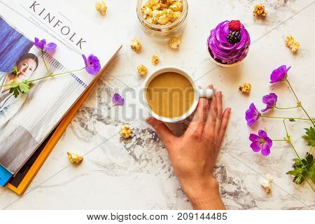 Kazakhstan Almaty - 26 AUGUST 2017: Popular magazine Kinfolk popcorn woman's hand with cup of coffee wild flowers and violet cupcake. Top view life style.