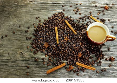 A cup of coffee and coffee beans anise and cinnamon on a wooden table. view from above