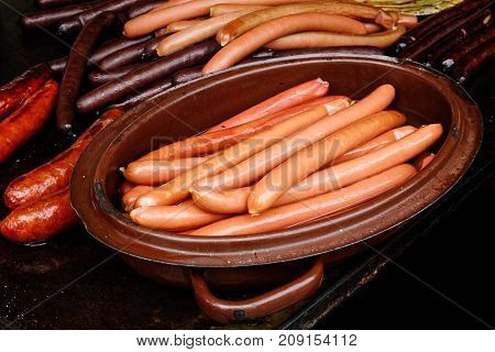 Boiled wiener sausages in metal pot next to grilled sausages on cast iron griddle.