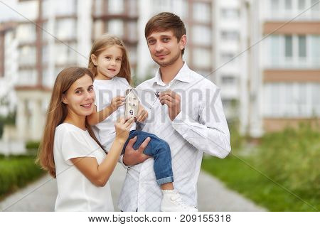 Lovely young family holding keys to their new apartment smiling joyfully posing outdoors. Husband and wife with their child holding keys to new house family happiness love concept